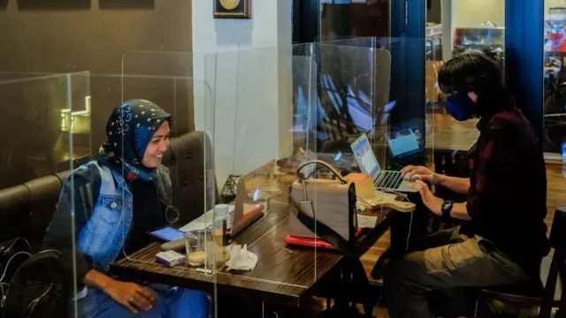 Pelanggan bersantap sambil bekerja di balik pemisah akrilik di Atjeh Connection, sebuah restoran yang baru dibuka kembali setelah kafe dan restoran dibuka kembali di tengah penyebaran wabah virus corona (COVID-19) di Jakarta, Indonesia pada 9 Juni 2020.