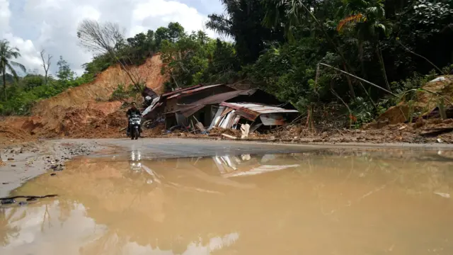 Pengendara sepeda motor melintas bekas tanah longsor yang menghancurkan rumah penduduk di Dusun Parsingkaman, Desa Pagaran Lambung I, Kecamatan Adiankoting, Kabupaten Tapanuli Utara, Jumat (26/12/2025). (Nanda Fahriza Batubara)