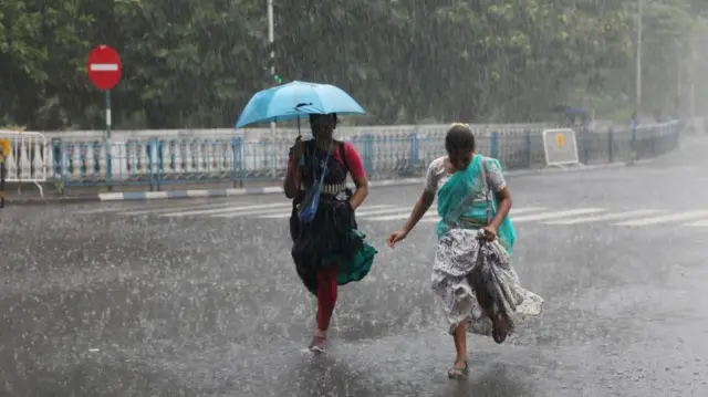 भारतको कोलकातामा वर्षा हुँदा बाटोमा हिँडेका दुई महिला 