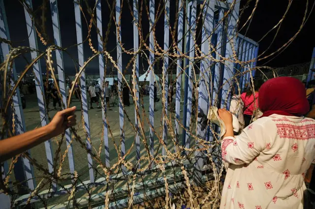 Seorang wanita melihat melalui gerbang kawat berduri saat orang-orang berkumpul di Bab Sebta, di perbatasan Maroko-Spanyol dekat wilayah kantong Spanyol Ceuta dan kota Fnideq di Maroko, pada 30 Juli 2026. Ratusan orang berkumpul di kota Fnideq di utara Maroko pada malam 30 Juli, menyusul rumor bahwa perbatasan dengan Ceuta di Spanyol telah dibuka, menurut seorang jurnalis AFP. Spanyol sebelumnya melaporkan sembilan kematian setelah ratusan migran memasuki wilayah kantong Afrika Utara dari Maroko, terutama dengan berenang. (Foto oleh