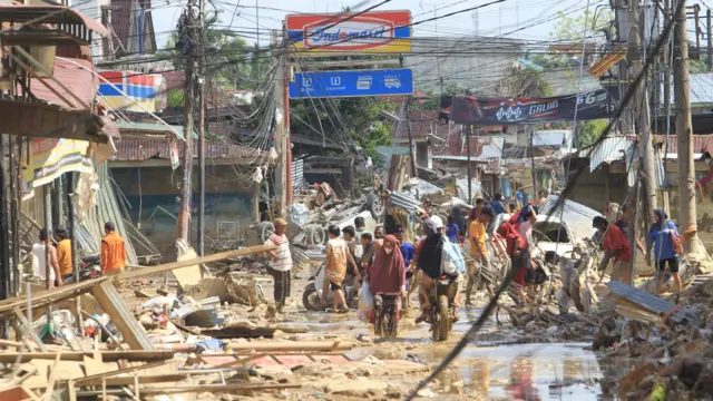 Sejumlah warga melintas di dekat puing-puing yang terbawa arus banjir di kawasan Desa Bukit Tempurung, Kota Kuala Simpang, Kabupaten Aceh Tamiang, Aceh, Rabu (3/12/2025).
