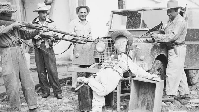 Чорно-біле фото показує опудало колишнього президента Гватемали Хакобо Арбенса, встановлене на джипі, тоді як чоловіки в капелюхах націлюють на нього рушниці. На опудалі є табличка з написом (іспанською): "Я повертаюся до Росії"