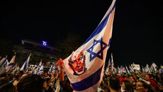 Una bandera israelí con la imagen de Netanyahu y una mancha roja sobre su cara