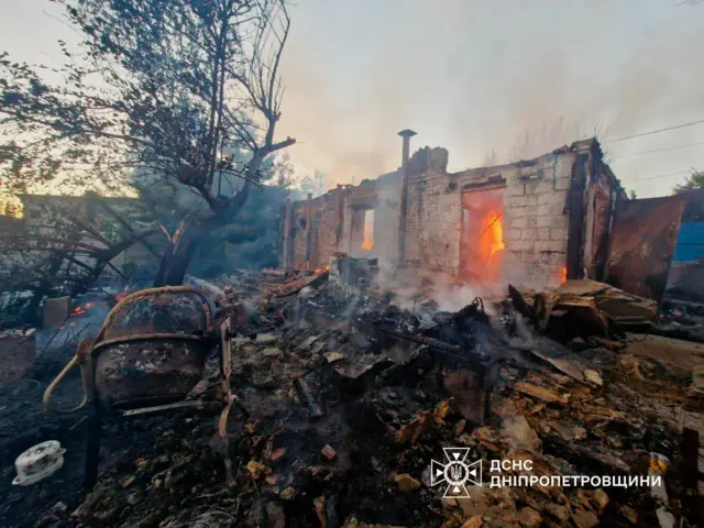 Згарище одноповерхового приватного будинку, всередині ще горить пожежа. Від будинку лишилися тільки стіни, довкола тліють деревʼяні дошки