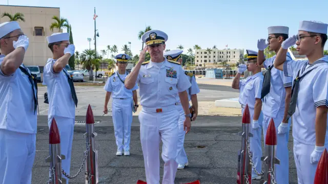 අද්මිරාල් ස්ටීව් කේලර් නාවික හමුදා නිලධාරීන් පිරිසකට ආචාරය කරමින් පැමිණෙන අයුරු.