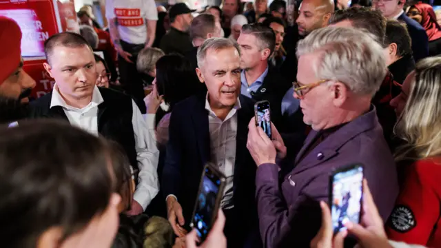 People are using their phones to take pictures of Liberal Party leader Mark Carney in a crowded bar in Ontario, during an election campaign stop
