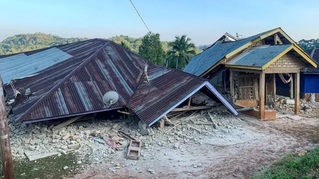 Uma casa desabou, de modo que apenas o telhado é visível, caído no chão.