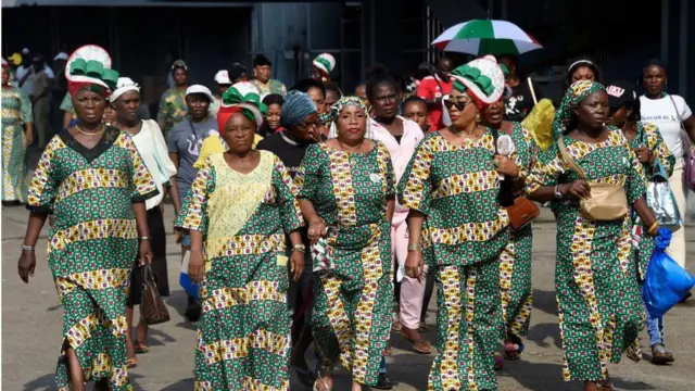 Nigerian women wearing the same green and yellow printed dresses walking the streets.