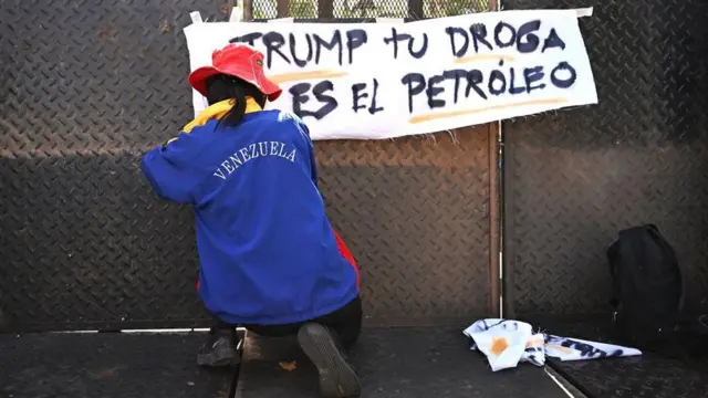 Seorang demonstran memasang poster bertuliskan "Trump, minyak adalah narkobamu" di depan Kedutaan Besar AS di Caracas, Venezuela, pada Sabtu (03/01).