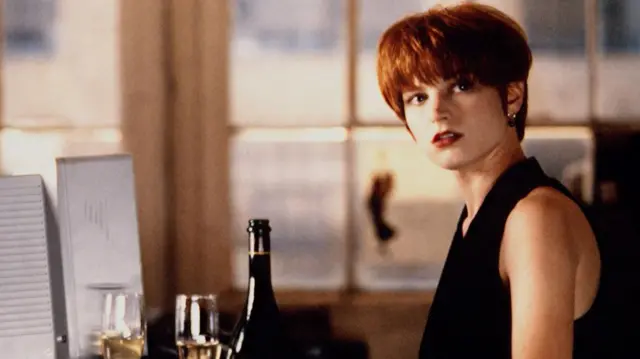 Bridget Fonda com cabelo curto vermelho, usando blusa preta
