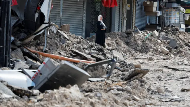 A Palestinian woman stands surrounded by rubble on a street in Jenin 