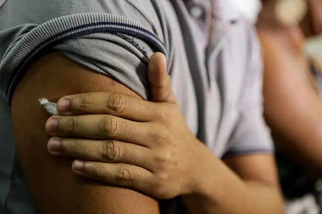 Pessoa com mão e adesivo no braço após tomar vacina