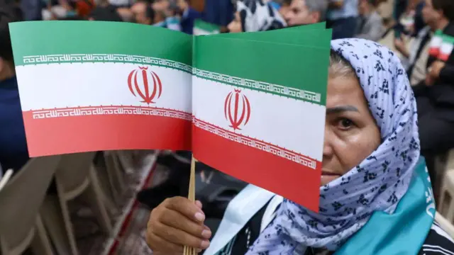 Seorang perempuan mengibarkan bendera nasional Iran saat presiden baru terpilih Masoud Pezeshkian mengunjungi kuil pendiri Republik Islam Ayatollah Ruhollah Khomeini di Teheran pada 6 Juli 2024.