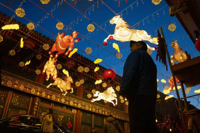 Человек стоит под светящимися матерчатами фигурами лошадей, бегущих по кругу