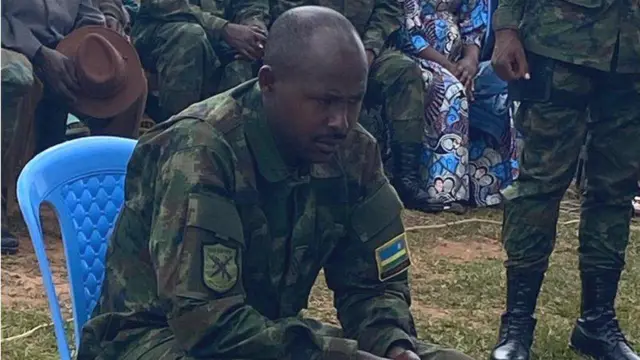 Sergeant Gervais Minani yicaye ku ntebe ya plastike, mu isomwa ry'urubanza rwe, mu murenge wa Karambi, mu karere ka Nyamasheke, mu majyepfo ashyira uburengerazuba bw'u Rwanda. Ifoto yo ku wa mbere, ku itariki ya 9 Ukuboza (12) mu mwaka wa 2024