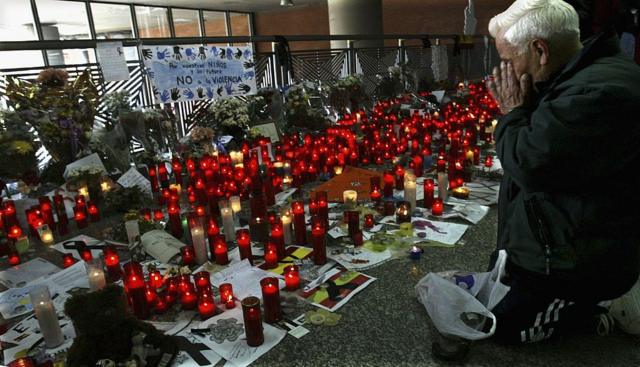 Um homem ajoelhado diante de flores e velas colocadas em memória das vítimas dos ataques do 11-M