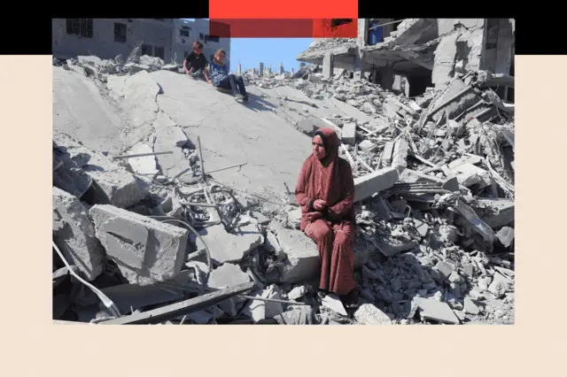 سيدة وطفل وطفلة يجلسون على ركام أحد المباني المدمرة في قطاع غزة.