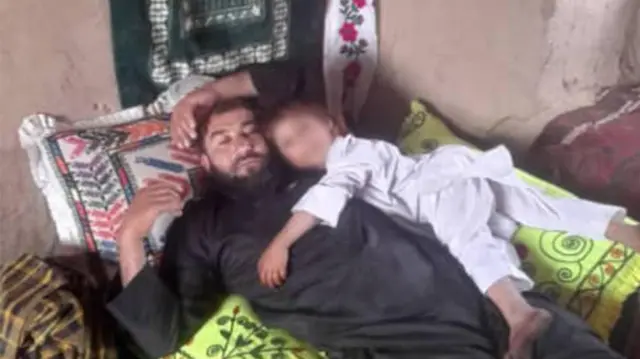 حیات الله په خپل کور کې پر بستر پروت دی په داسې حال کې چې د هغه یو کوچني ماشوم ځان پرې اچولی دی.