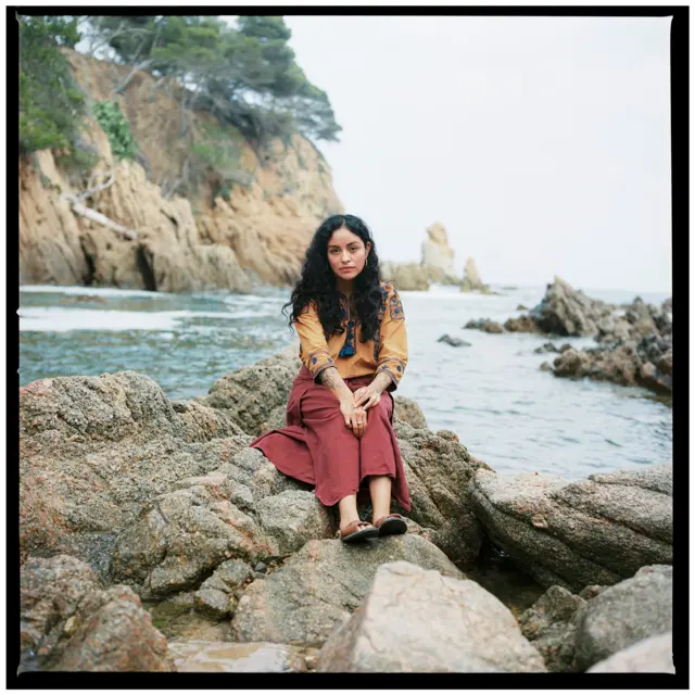 Retrato de Clyo Mendoza sentada en una piedra en una playa.