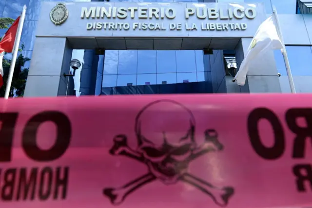 Fachada donde se lee "Ministerio Público", "Distrito Fiscal de La Libertad". Frente ella, una cinta plástica con una calavera y dos tibias. 