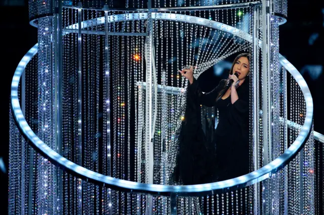 žena među staklenim perlama u crnoj haljini peva