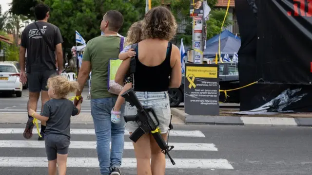 ጠመንጃ አንግታ ልጇን አቅፋ በመንገድ ላይ የምትጓ እስራኤላዊት እናት