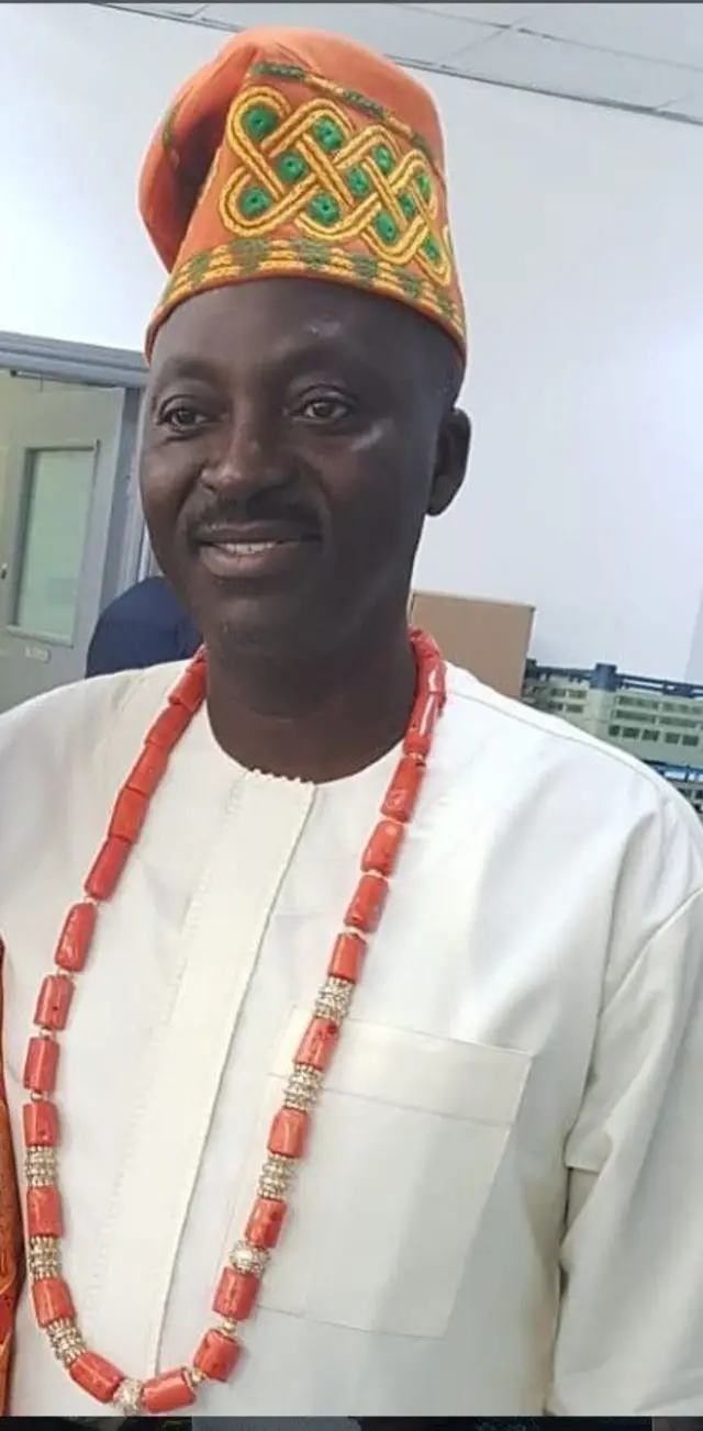 Oloogbe Teslim Ajimobi wọ agbada asọ leesi toke tilẹ ati fila asọ oke alawọ goolu, o si fi ilẹkẹ iyun sọrun, o n rẹrin