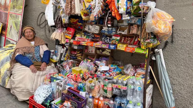 Mulher com trajes típicos sentada ao ladooutra vitória local betnacionalbarraca com doces e refrigerantes