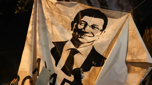Spanduk Ekrem Imamoglu dengan seseorang yang mengenakan penutup wajah dan kerudung berdiri di depannya