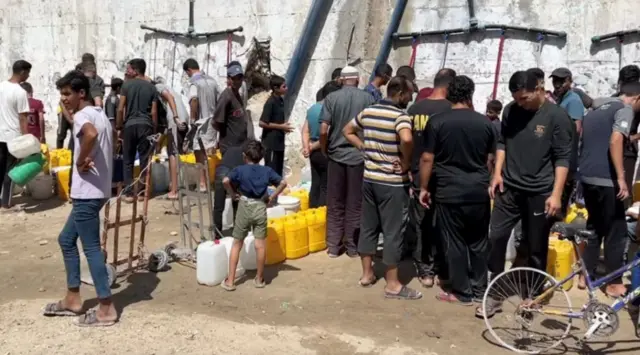 مجموعة من الرجال والأطفال يتجمعون عند نقطة لتوزيع المياه