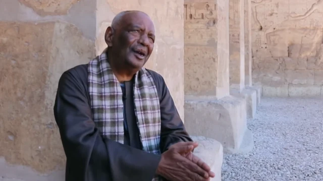 حورس - مرافق دوروثي إيدي بعباءة داكنة وشال يجلس في مقابلة أمام باب معبد أبيدوس