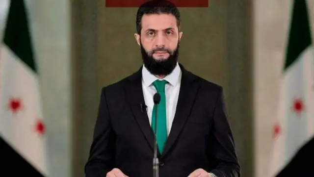 احمد شرع کت و شلوار سیاه و کراواتی سبز رنگ در حال سخنرانی