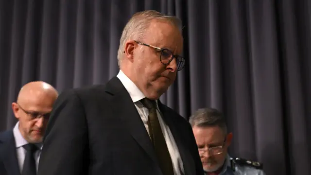 澳洲总理阿尔巴尼斯(中)在坎培拉会见记者后离开,神情肃穆(14/12/2025)