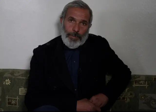 حسين بلحية وشعر أبيض يرتدي قميص كحلي وجاكيت أسود ويجلس على فراش بلون زيتي وذهبي