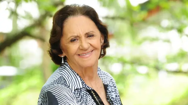 Laura Cardoso sorri para a câmera, usando uma blusa estampada, em meio à vegetação.