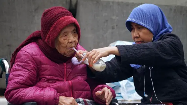 一名外佣正喂老人喝奶。