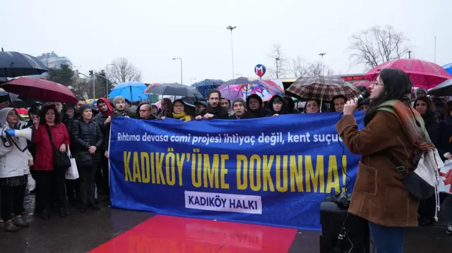 Eylemciler yağmurun altında şemsiyeler ile duruyor. Ortada üzerinde "Kadıköy'üme dokunma" yazan büyük bir pankart var. 