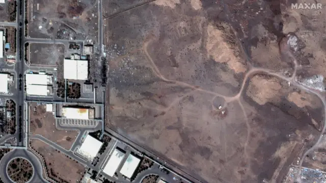 منطقة سوداء مليئة بالأنقاض بجوار مبانٍ في منطقة نطنز. تمتد شبكة من الطرق المستقيمة بين المباني، مع وجود دوار أسفل يسار الصورة.