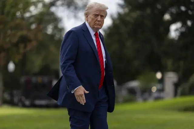 Trump com olhar sério caminhando em gramado