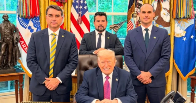 Foto do senador Flávio Bolsonaro, Donald Trump (sentado), Eduardo Bolsonaro (do lado direito) e Paulo Figueiredo sentado atrás de Trump. Todos no salão oval da Casa Branca. 