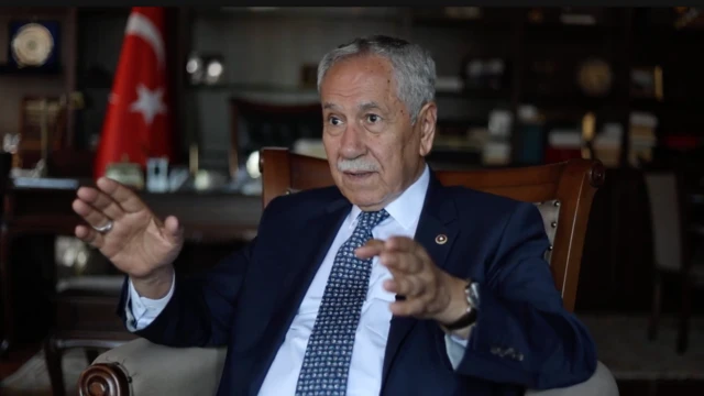 Bülent Arınç, Ankara Hamamönü'ndeki ofisinde, BBC Türkçe'nin sorularını yanıtlıyor. Üzerinde lacivert bir takım elbise var. Bir koltukta konuşuyor. Arkada çalışma odasının rafaları, bir masa ve bir Türk bayrağı görülüyor.