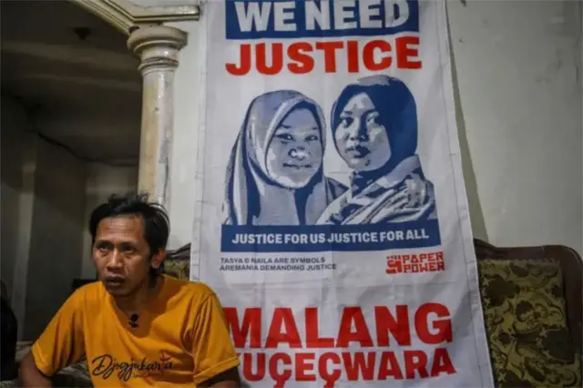 Devi Athok Yulfitri di depan spanduk dengan foto dua mendiang putrinya, yang tewas bersama ibu mereka dalam tragedi Kanjuruhan di Malang, Jawa Timur, pada 1 Oktober 2022.