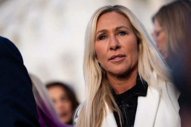 Marjorie Taylor Greene con una camisa negra y una chaqueta blanca y el cabello rubio suelto
