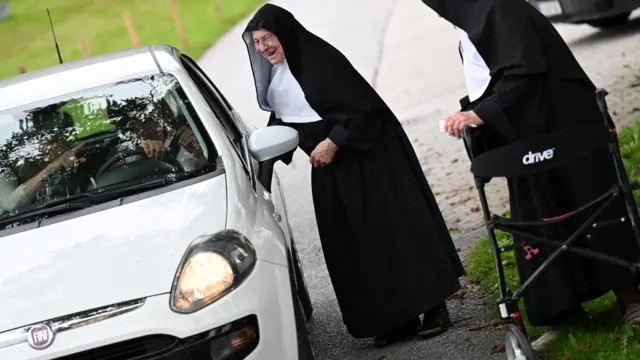 دو راهبه کنار ماشینی ایستاده‌اند و با سرنشینان حرف می‌زنند و می‌خندند. 