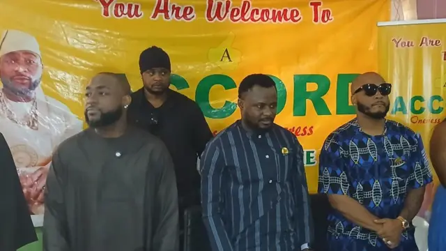 Davido wọ asọ toke tilẹ alawọ dudu, ko de fila, o fi yẹri si eti, o si duro laarin awọn ẹmẹwa rẹ, ti ami idamọ ẹgbẹ oselu Accord si wa lẹyin wọn