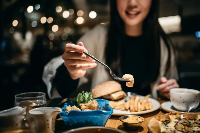 Smiling young woman enjoying her meal and sharing her food in a restaurant