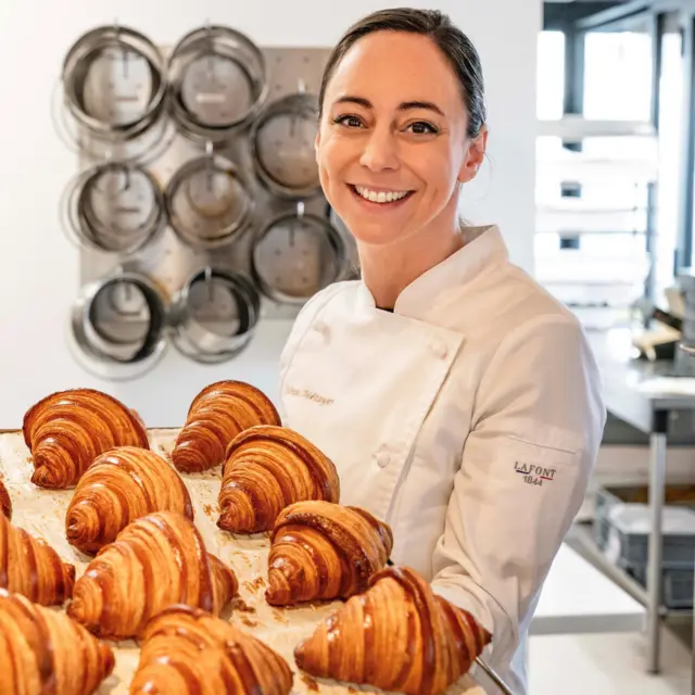 الطاهية المتخصصة بالحلويات نينا ميتايي من فرنسا تحمل لوحا من الكرواسان المخبوز وترتدي زي الشيف الأبيض