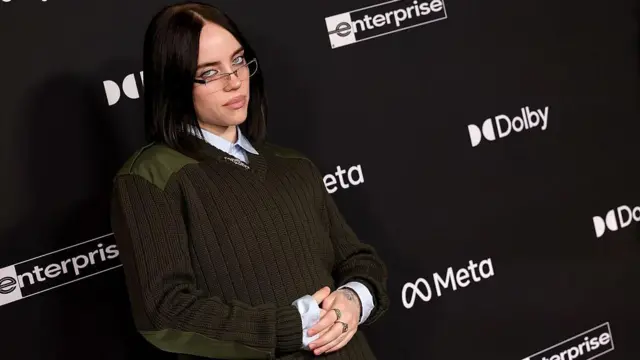 Billie Eilish üzerinde haki renkli br kazakla poz veriyor, 1 Aralık 2025