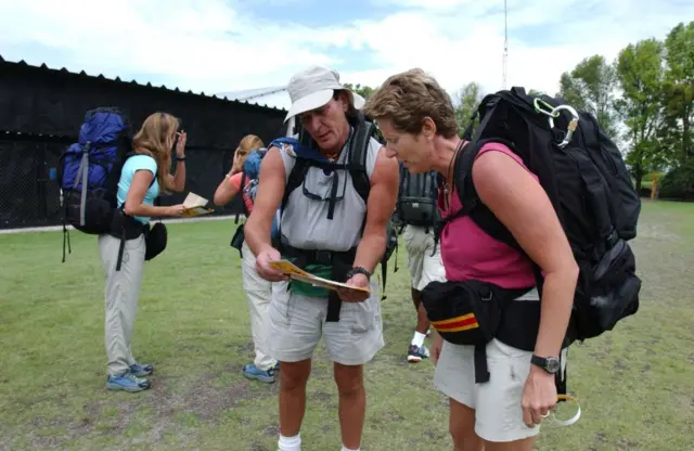 Um casal com duas mochilas grandes nas costas olhando um folheto em um espaço verde