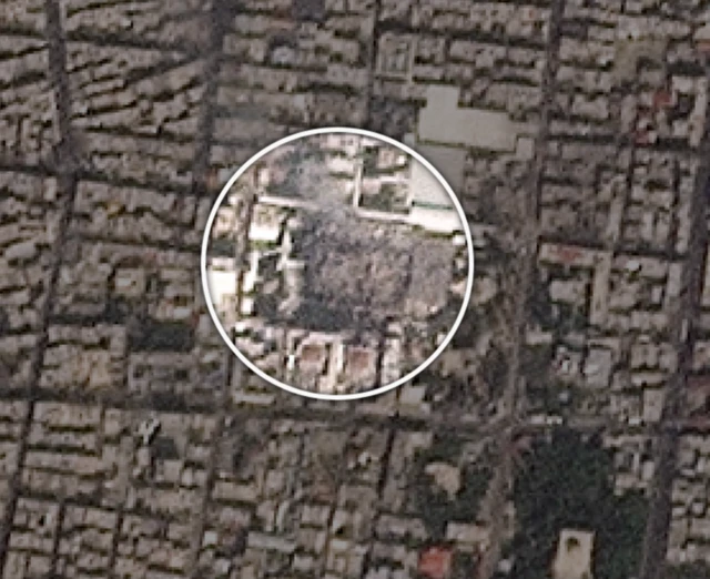 Супутниковий знімок щільно забудованого міського району. У центрі кадру в колі виділена ділянка, де видно значну зону руйнувань: будівлі або внутрішній двір комплексу виглядають сильно пошкодженими чи частково знищеними.